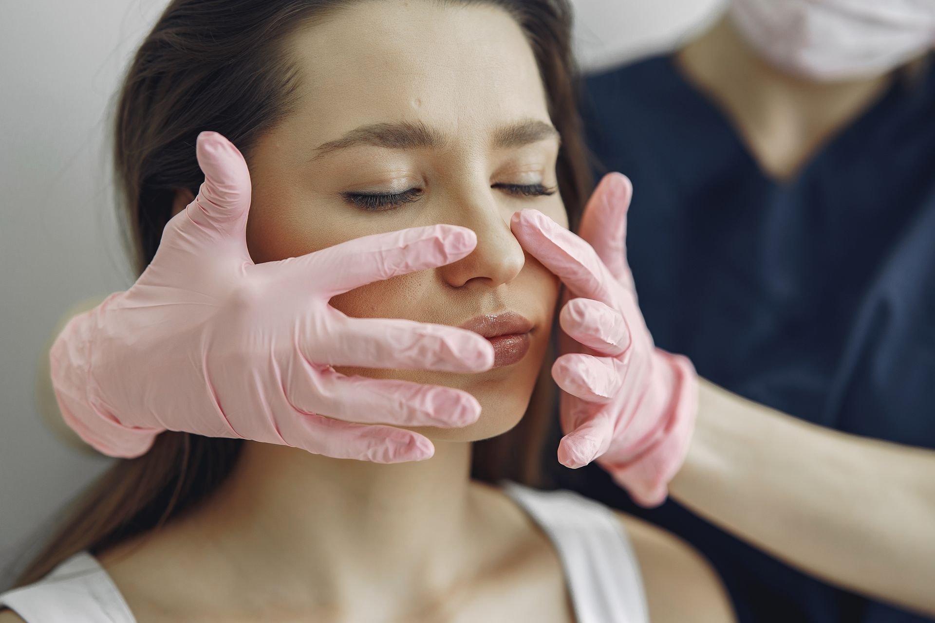 DermAesthetics practitioner in pink clinical gloves examining a patient's face during an aesthetic skin clinic consultation